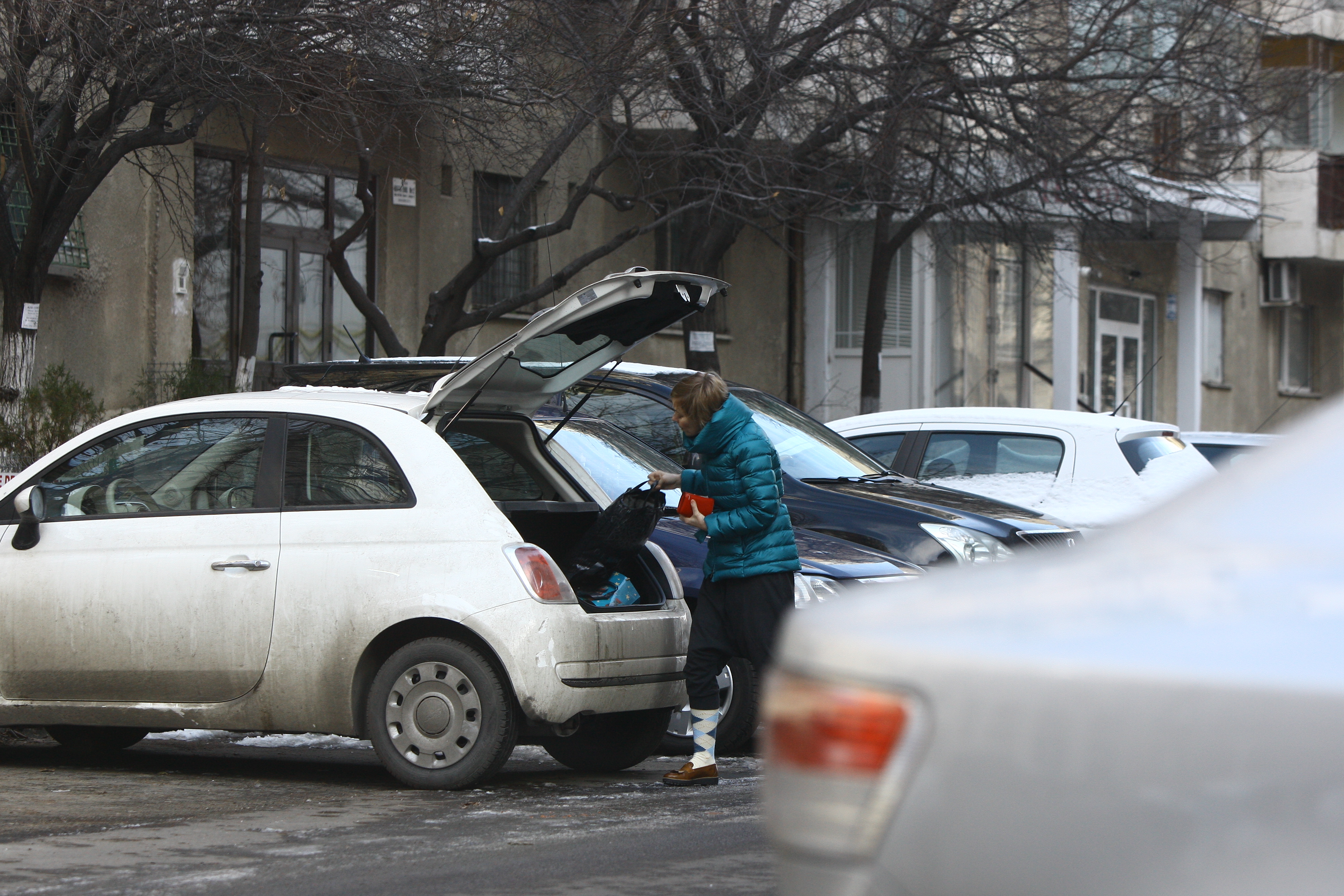 Prezentatoarea de la TVR ia o sacosa din portbagajul masinii sale si intre in scara de bloc