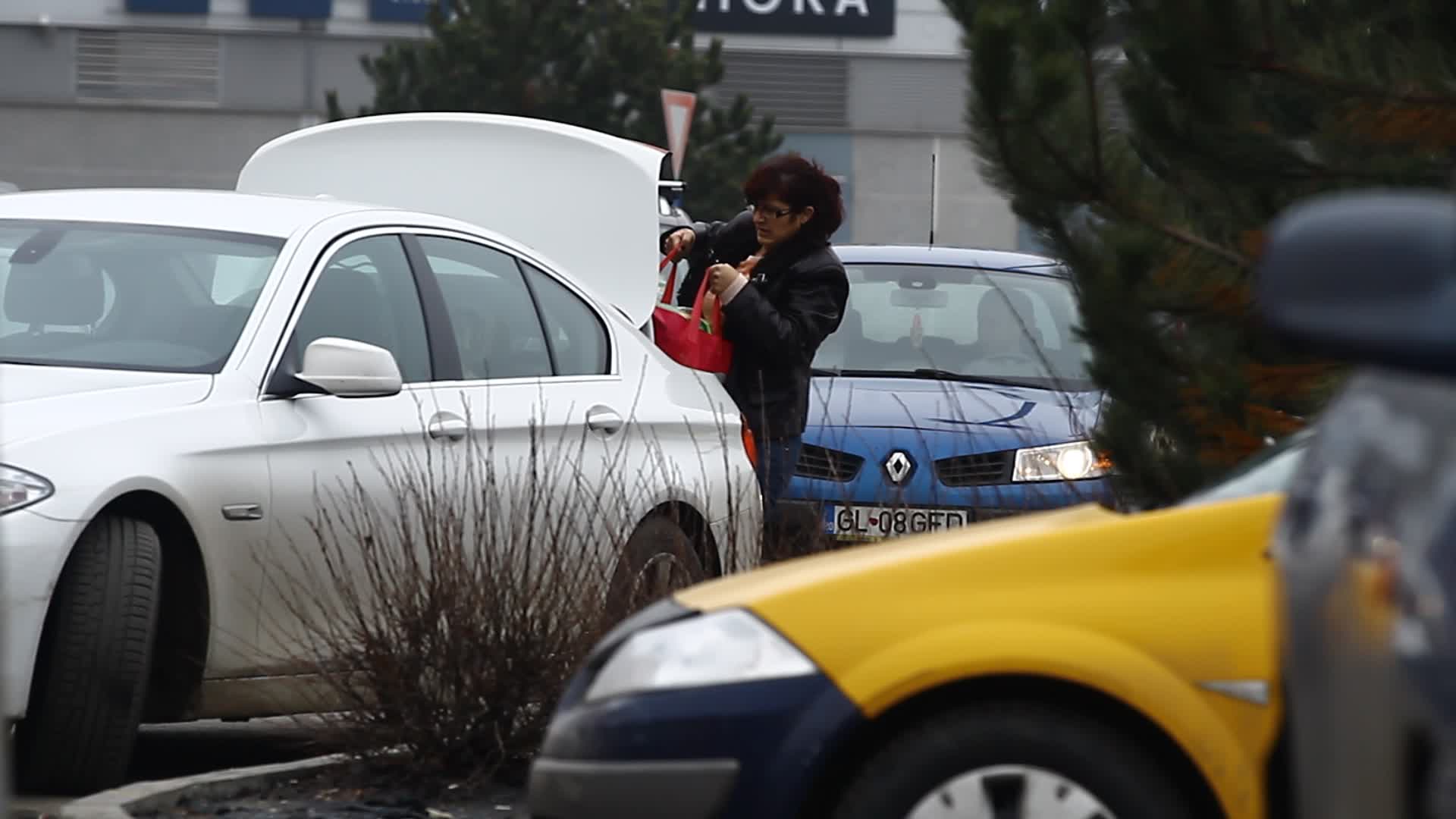 Asistenta incarca provizile cumparate in portbagajul masinii