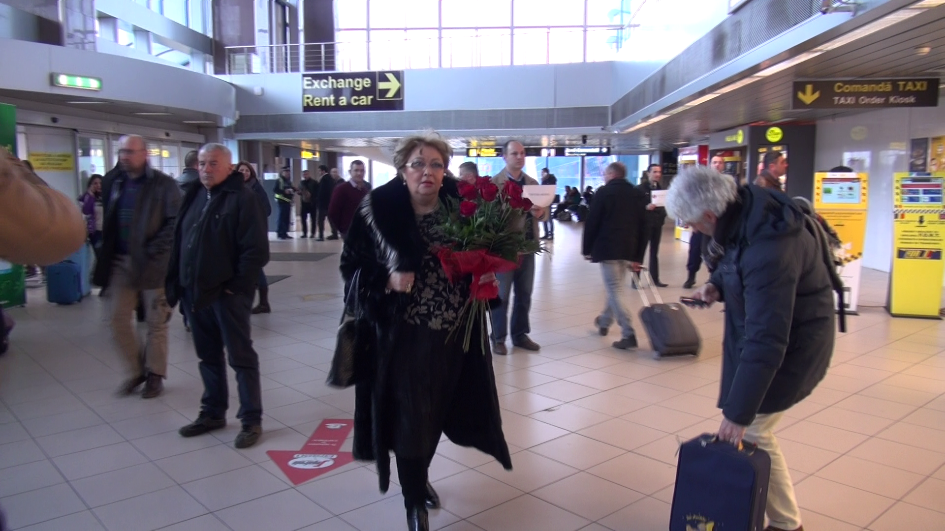 Mama Oanei se indreapta cu un buchet de flori spre poarta de iesire