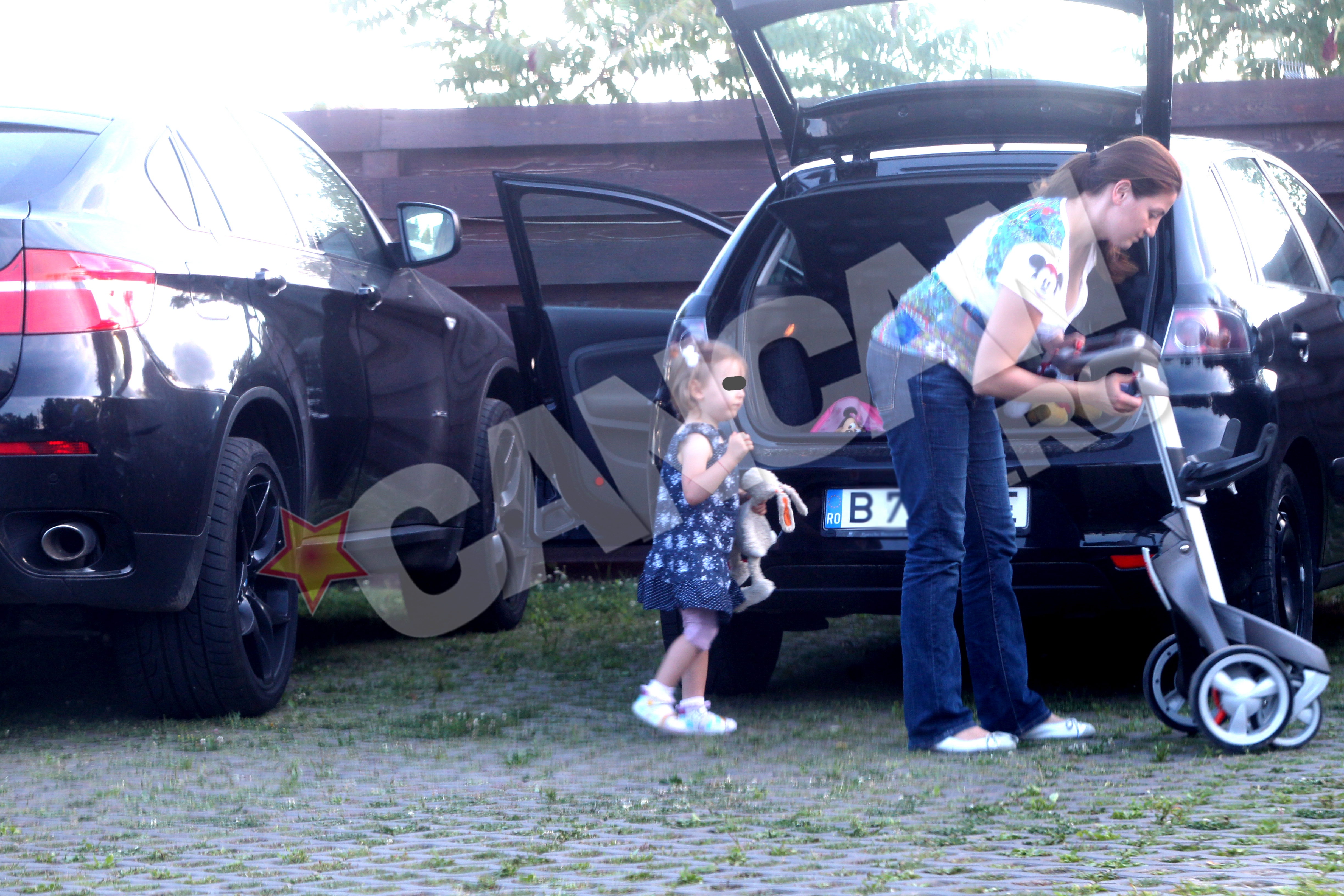 Desi nu o ajuta nimeni, Adriana manuieste cu indemanare obiectele din portbagaj si scoate un carut pentru fetita cea mica