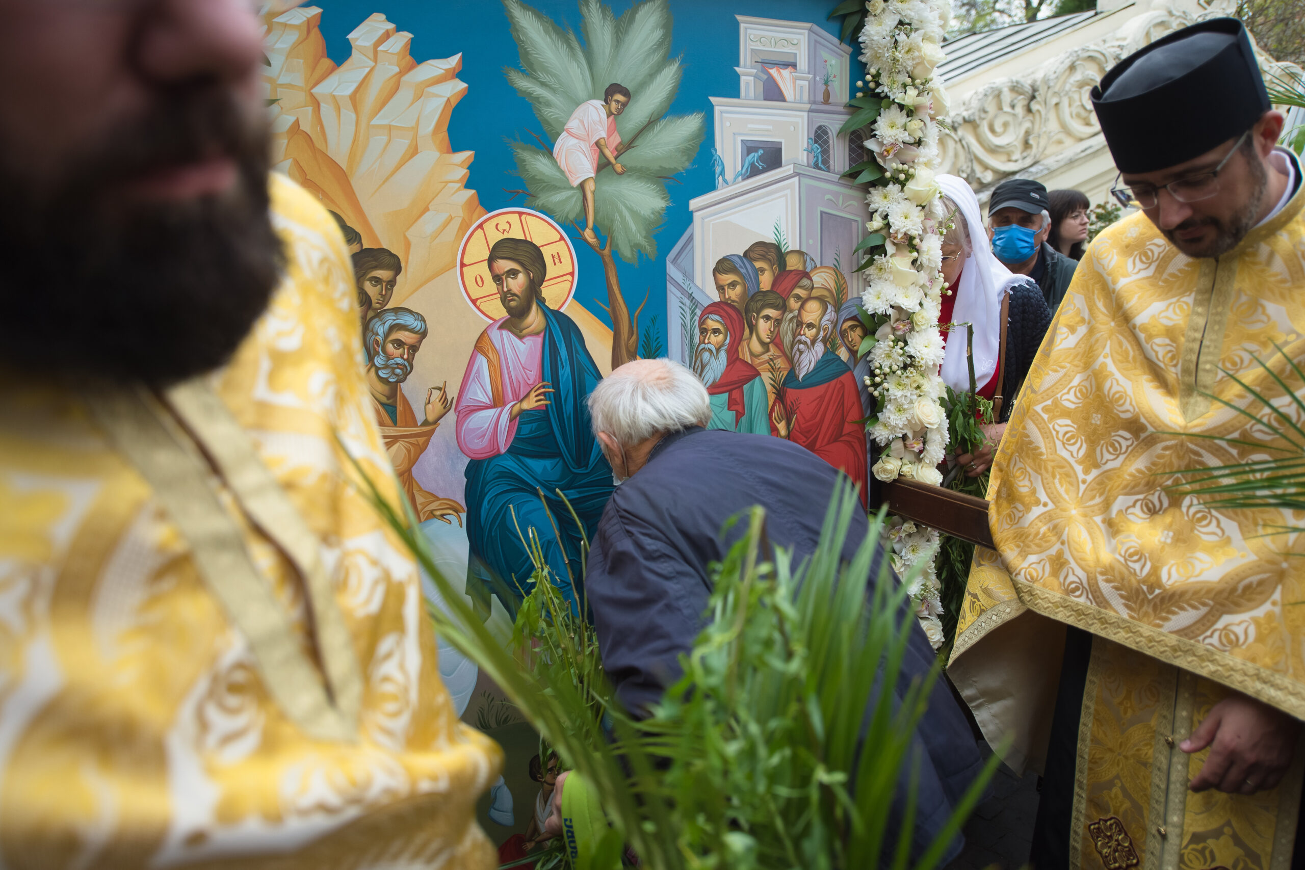 un barbat care saruta o icoana, intre doi preoti, cu frunze