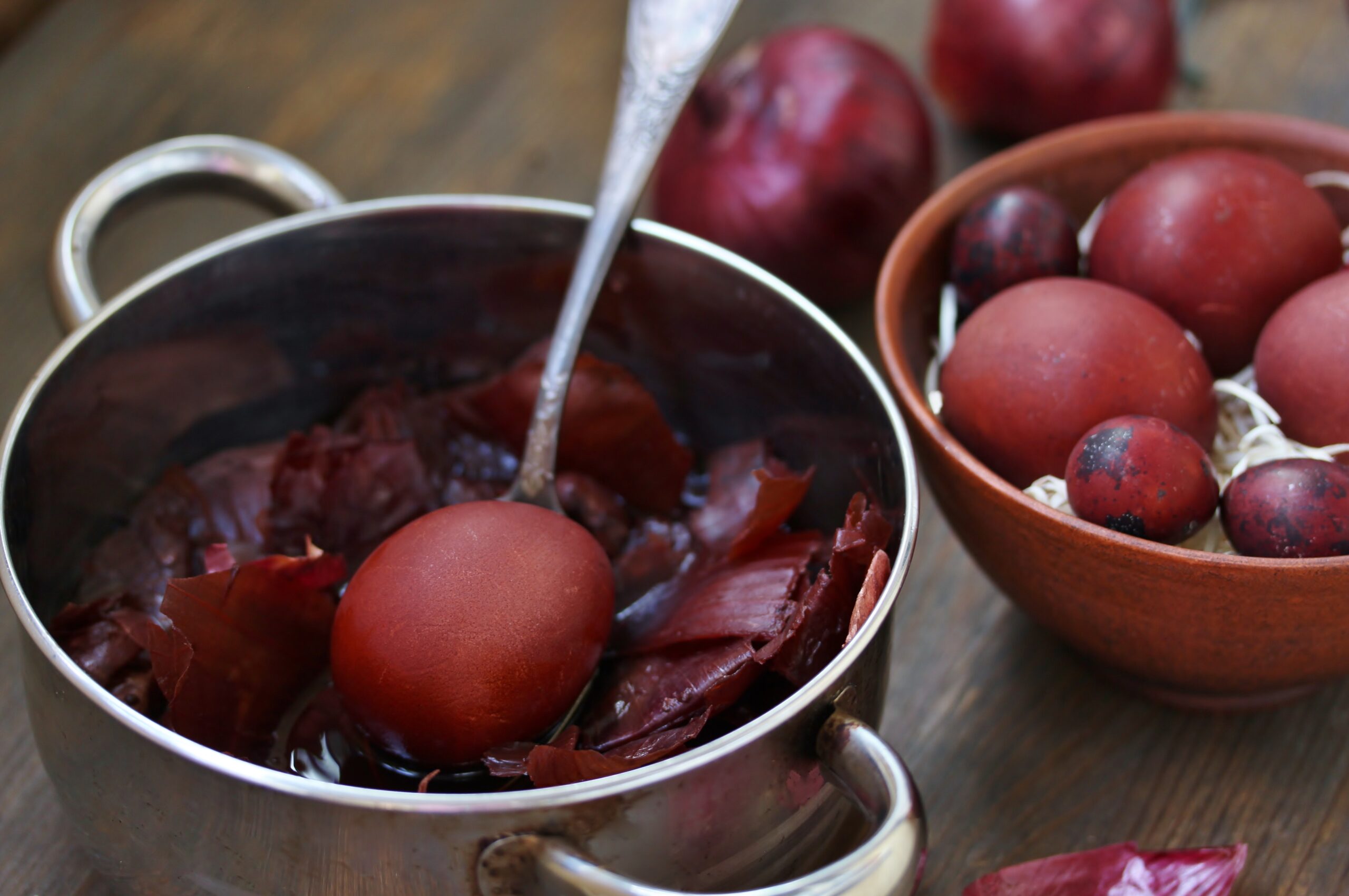 cratita cu lingura de fier in ea, ou rosu fiert, castron cu ceapa rosie, oua si foi de ceapa rosie pe o masa de bucatarie