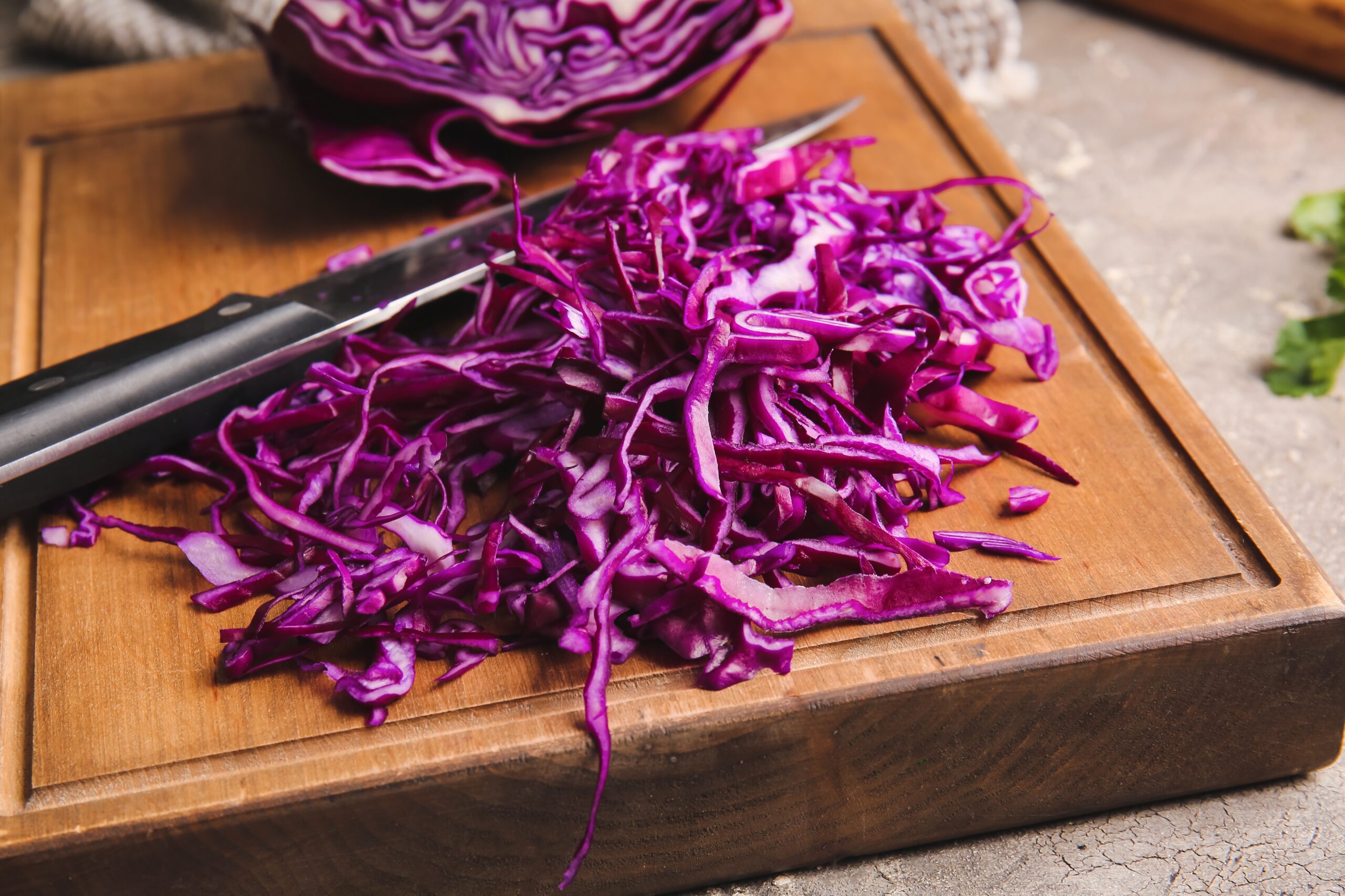 un tocator din lemn, cu varza rosie tocata pe el, un cutit din inox